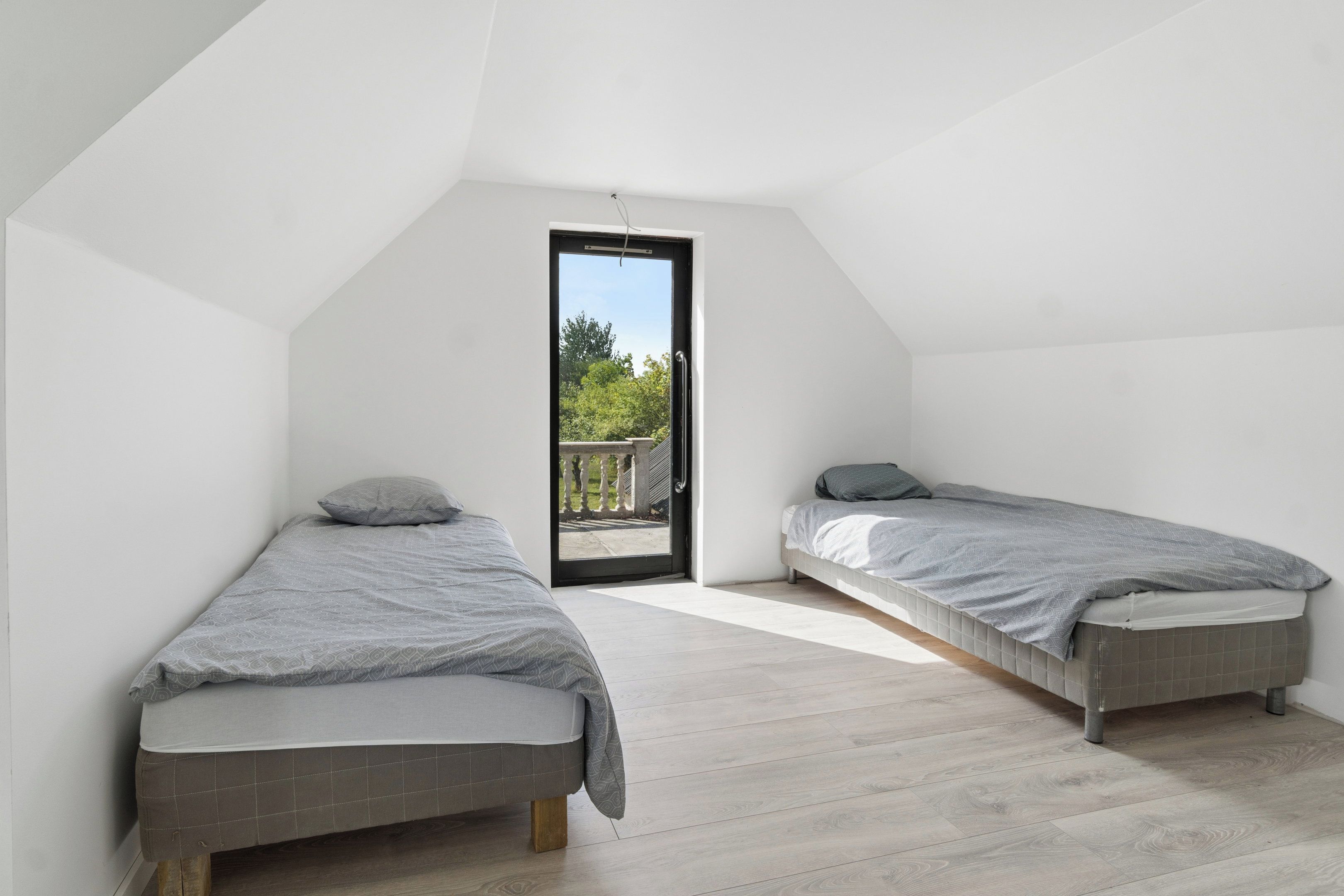 A small, modern bedroom with two single beds, a wooden floor, and a balcony door leading to an outdoor area.