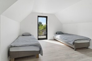 Une petite chambre moderne avec deux lits simples, un plancher en bois et une porte-fenêtre donnant sur un espace extérieur.
