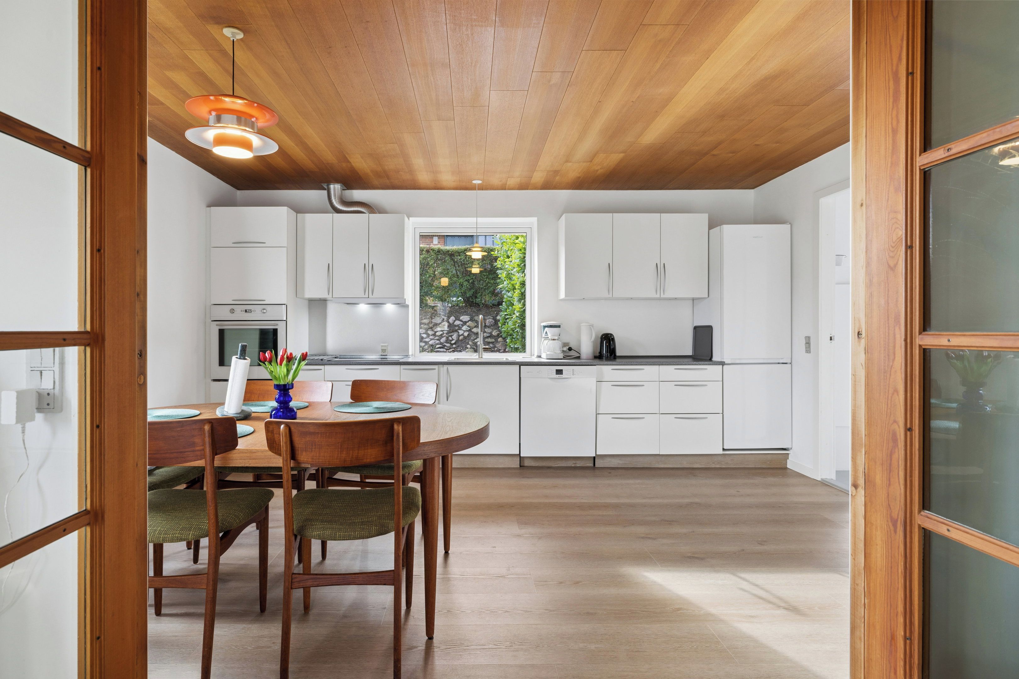 Una cocina moderna con armarios blancos, una mesa de comedor con sillas y un ventanal con vistas al verdor.