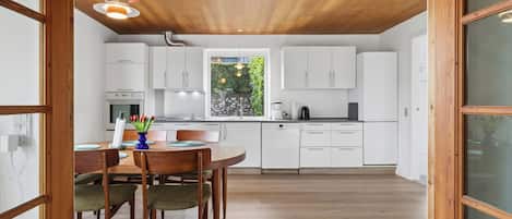 Una cocina moderna con armarios blancos, una mesa de comedor con sillas y un ventanal con vistas al verdor.