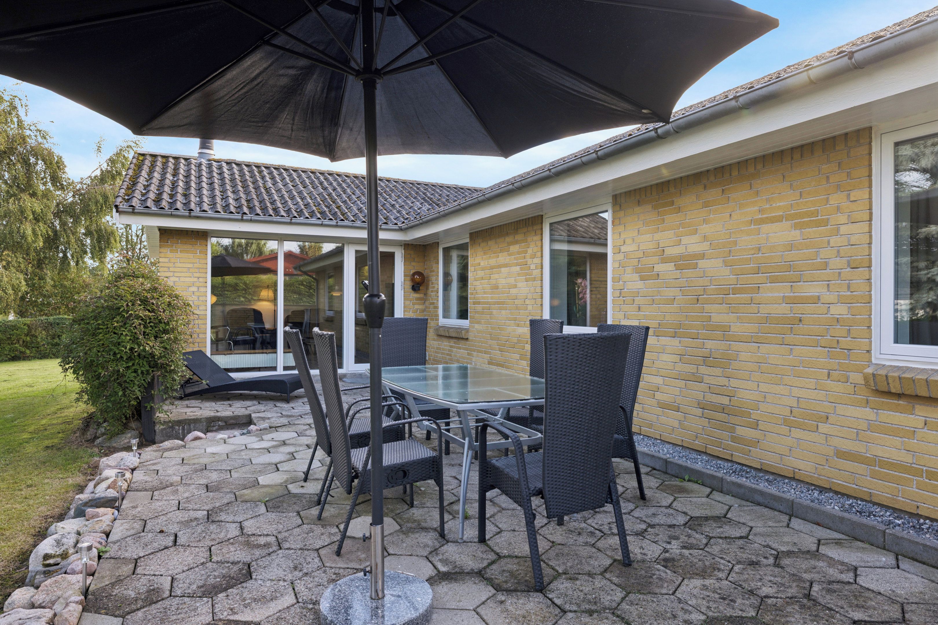 Une terrasse extérieure avec une table et des chaises en verre, un parasol noir et un mur en briques.