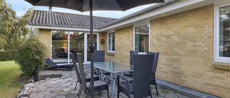 An outdoor patio with a glass table and chairs, a black umbrella, and a brick wall.
