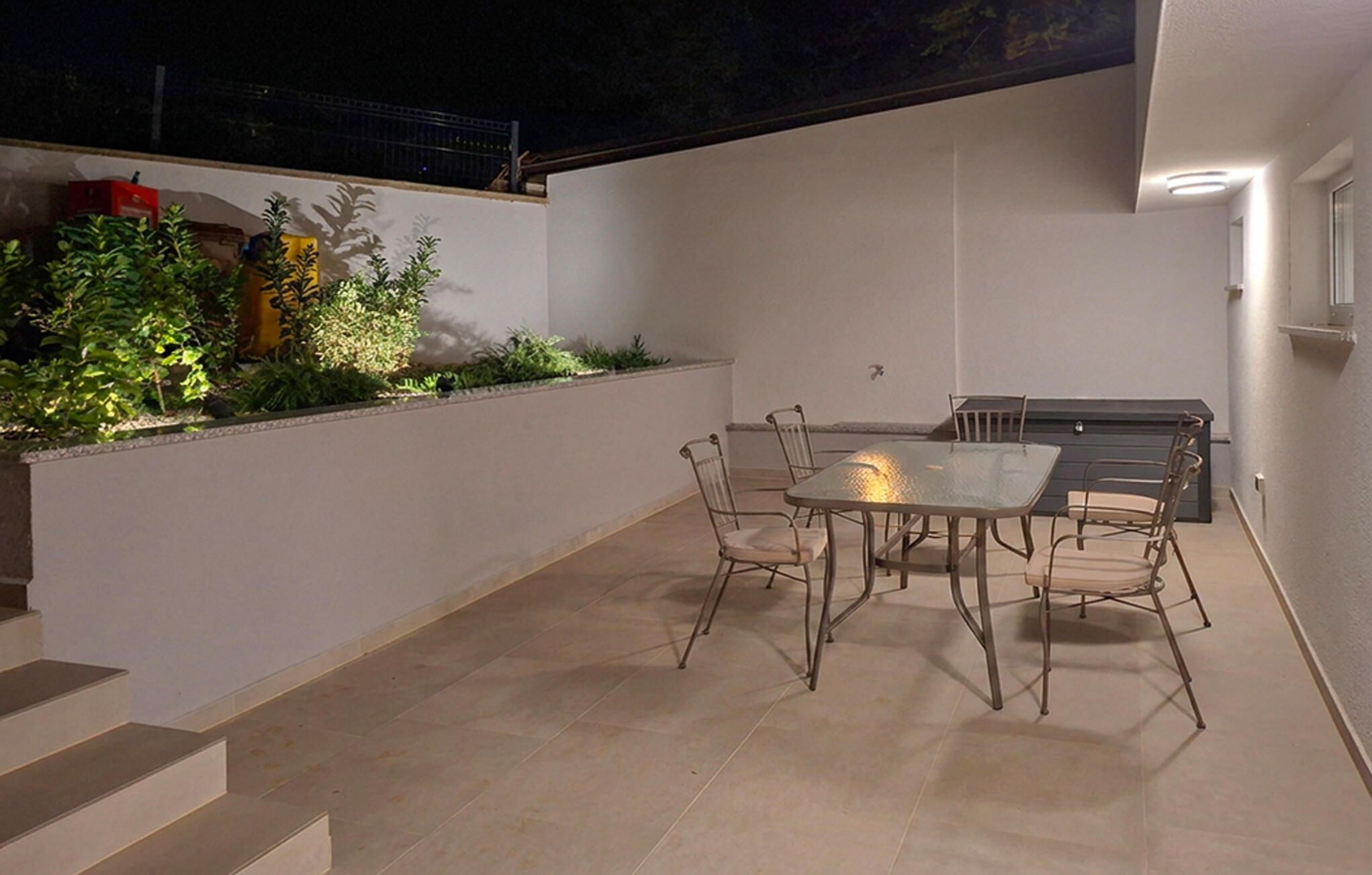 An outdoor patio with a table and chairs, a grill, and a small garden area with plants.