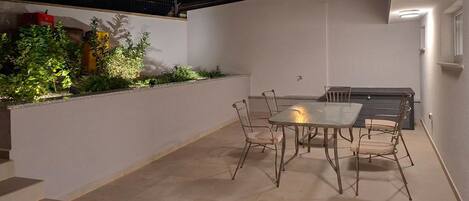 Un patio al aire libre con mesa y sillas, una parrilla y un pequeño jardín con plantas.
