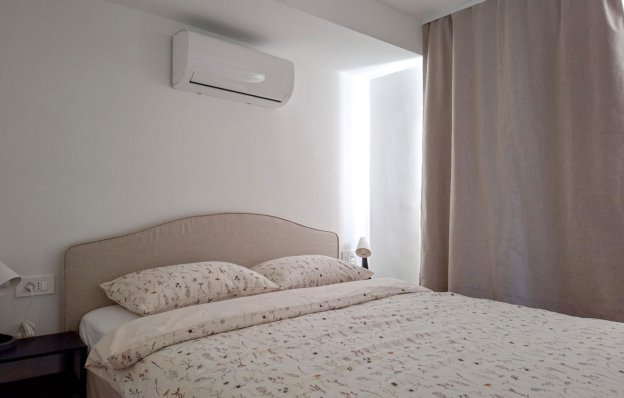 Ein Schlafzimmer mit einem Bett, einem Nachttisch, einer Lampe und einer Klimaanlage.