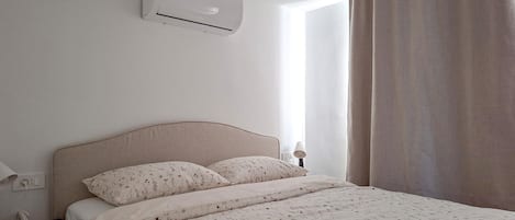 Ein Schlafzimmer mit einem Bett, einem Nachttisch, einer Lampe und einer Klimaanlage.