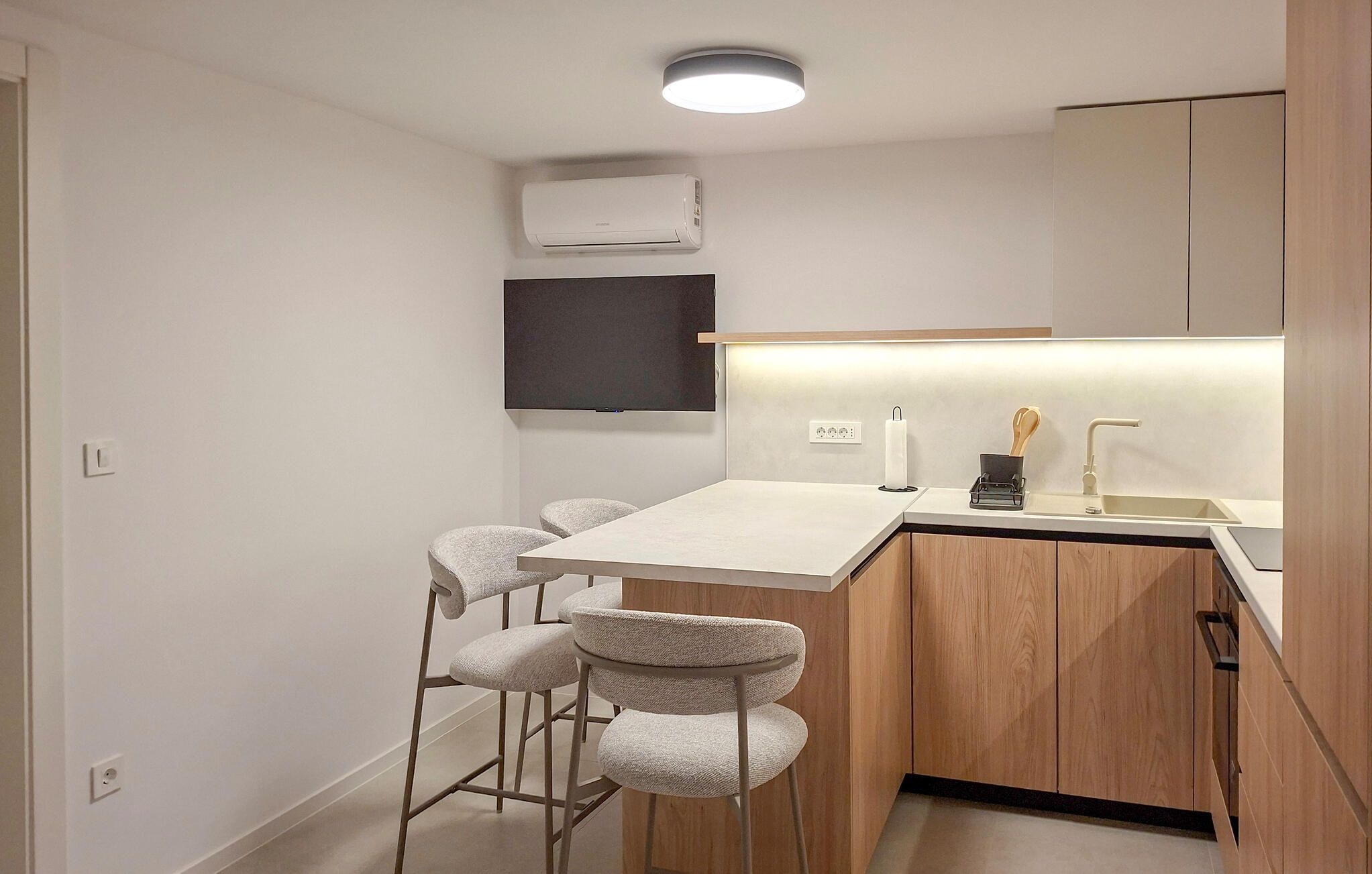 A compact kitchen with a bar area, wooden cabinets, a built-in TV, and a modern light fixture.