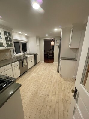 A modern kitchen with white cabinetry, a stainless steel range, and a wooden floor. - Quaint 2-bedroom Cottage Walking Distance to the Beach (Yarmouth)
