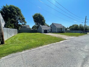 A residential property with a well-maintained lawn, a gravel driveway, and a wooden fence. - Quaint 2-bedroom Cottage Walking Distance to the Beach (Yarmouth)