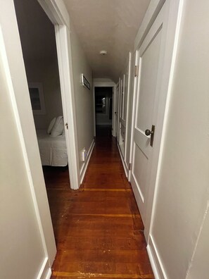 A hallway with wooden flooring, white doors, and a bed with a white bedspread. - Quaint 2-bedroom Cottage Walking Distance to the Beach (Yarmouth)