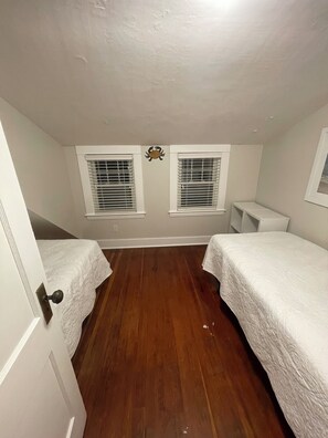 A small, narrow room with two beds, a wooden floor, and a ceiling with a decorative crab. - Quaint 2-bedroom Cottage Walking Distance to the Beach (Yarmouth)