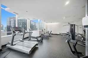 Ein Fitnessstudio mit Laufbändern, Crosstrainern und Kraftgeräten, das große Fenster mit Blick auf die Stadt hat.