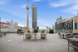 Una terraza en la azotea con mesas y sillas, vistas a la Torre CN y edificios modernos al fondo.