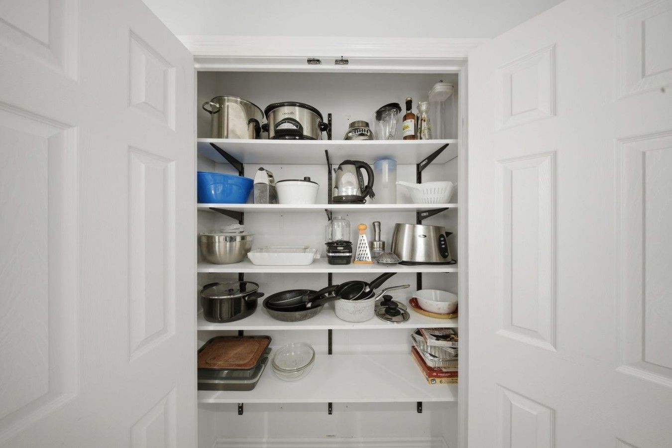 A white pantry with shelves containing various kitchen items like pots, pans, and containers.