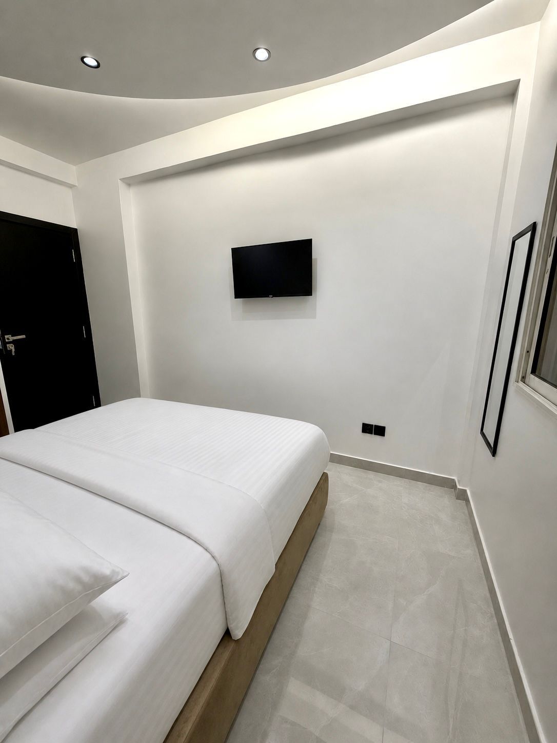 A modern bedroom with a bed, a mounted TV, and a door.