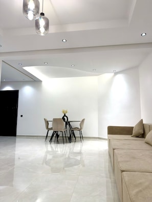 A modern living room with a sofa, a dining table with chairs, and recessed ceiling lighting. - 2bed.bathroom.2pool (Marrakech)