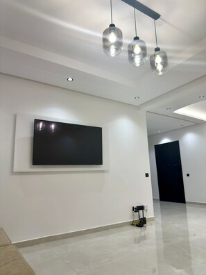 A modern interior with a flat-screen TV mounted on the wall, recessed ceiling lights, and a tiled floor. - 2bed.bathroom.2pool (Marrakech)