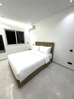 A modern bedroom with a bed, white bedding, a window, and an air conditioning unit. - 2bed.bathroom.2pool (Marrakech)