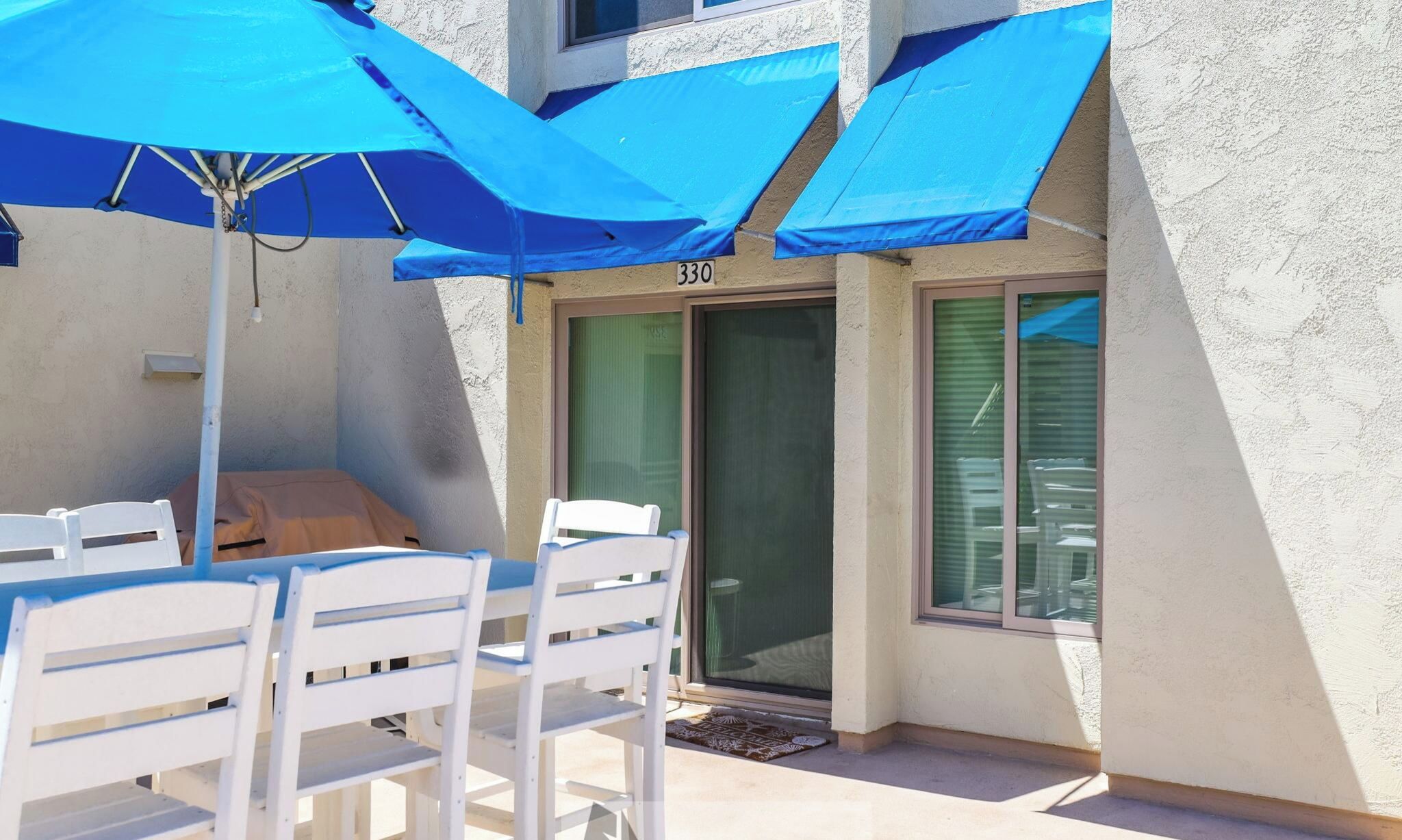 A patio area with white chairs and blue umbrellas, a door labeled '330', and a window with blinds.