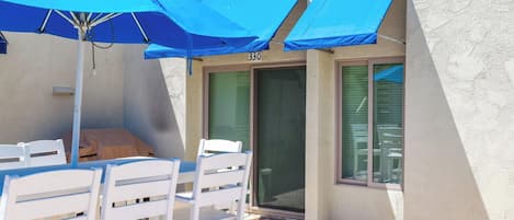 A patio area with white chairs and blue umbrellas, a door labeled '330', and a window with blinds.
