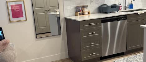 Una cocina moderna con gabinetes grises, lavavajillas de acero inoxidable y salpicadero de azulejos blancos.