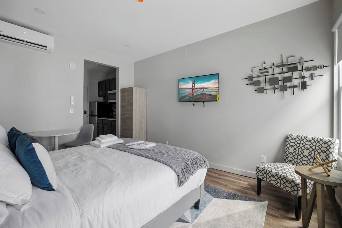 Una moderna camera d'hotel con un letto, una TV, un'opera d'arte a parete e una zona salotto.