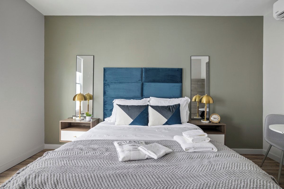 A modern hotel room with a large bed, two bedside tables, a nightstand, a chair, and a large mirror.