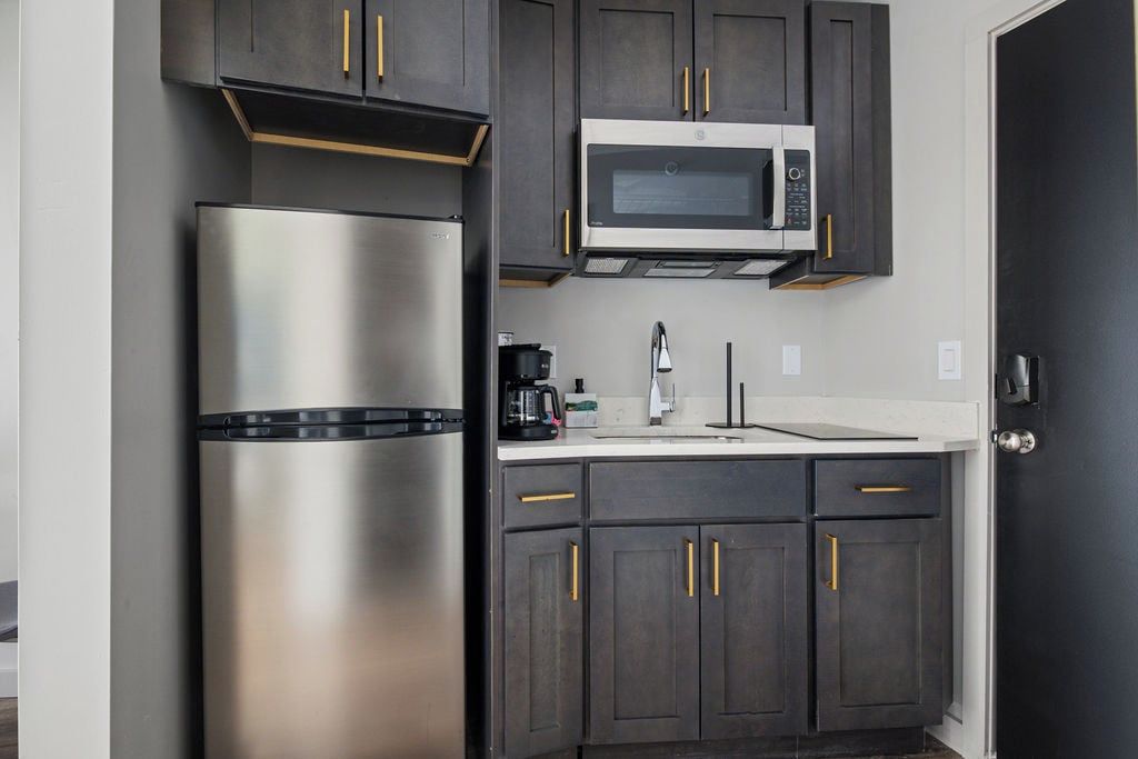 A kitchen with dark cabinets, a stainless steel refrigerator, a microwave, and a coffee maker.