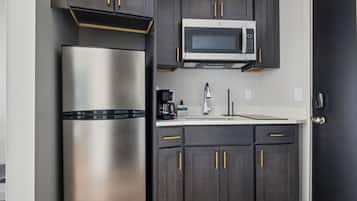 A kitchen with dark cabinets, a stainless steel refrigerator, a microwave, and a coffee maker.