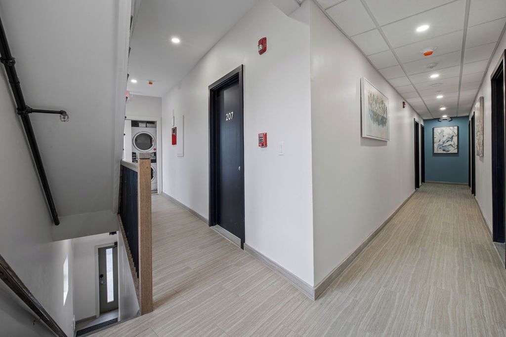 A hotel corridor with a staircase, a door labeled '207', and a laundry room in the background.