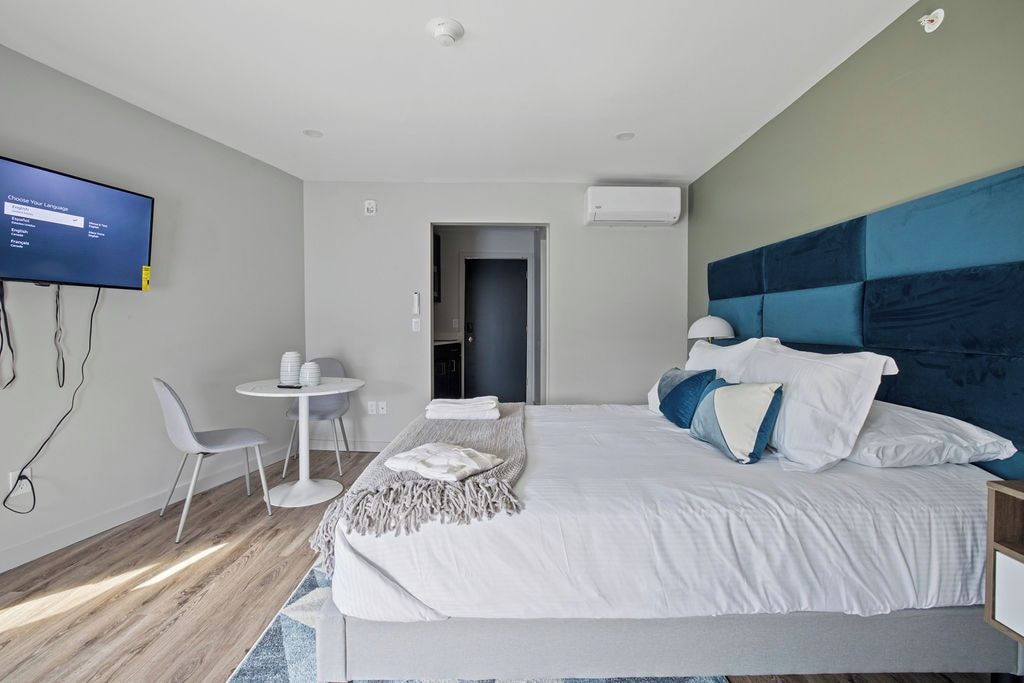 A modern hotel room with a large bed, a flat-screen TV, a small round table, and a seating area.