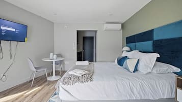 A modern hotel room with a large bed, a flat-screen TV, a small round table, and a seating area.