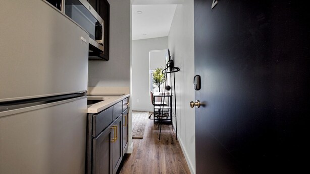 A narrow kitchen with a wooden floor, a dining area with a table and chairs, and a black door with a brass handle. - The Columbus Hotel - The Residence Studio - 89-206 (Middletown)