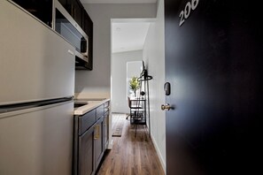 A narrow kitchen with a wooden floor, a dining area with a table and chairs, and a black door with the number 206 visible. - The Columbus Hotel - The Residence Studio - 89-206 (Middletown)