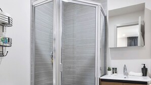 A modern bathroom with a glass-enclosed shower, a white toilet, a wooden vanity, and a small mirror. - The Columbus Hotel - The Residence Studio - 89-206 (Middletown)