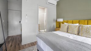 A hotel room with a bed, a nightstand, a lamp, and an air conditioning unit. - The Columbus Hotel - The Residence Studio - 89-206 (Middletown)