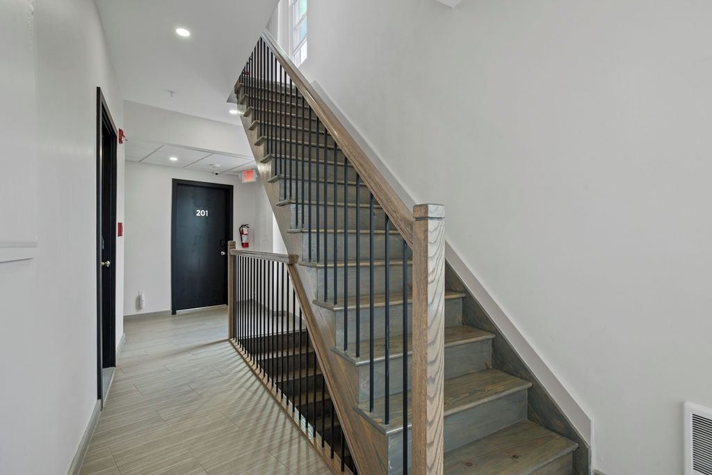 A staircase with a wooden handrail and metal balusters, leading to a door marked '201'.
