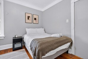 Ein Schlafzimmer mit einem Bett, einem Nachttisch, einer Wanduhr und zwei gerahmten Bildern.