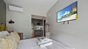 Ein Schlafzimmer mit einem Bett, einem Flachbildfernseher, einem Schreibtisch und einer kleinen Küche im Hintergrund.
