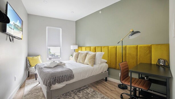 Ein modernes Schlafzimmer mit Bett, Nachttisch, Stuhl, Schreibtisch und einem Fenster.