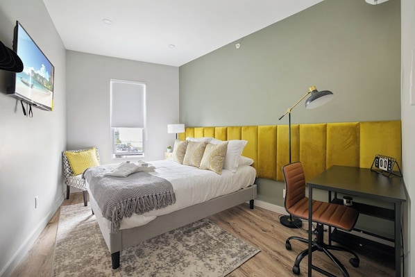 Ein modernes Schlafzimmer mit Bett, Nachttisch, Stuhl, Schreibtisch und einem Fenster.