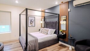 A four-poster bed with a grey headboard, a bedside table with a lamp, and a wall-mounted air conditioner. - The Columbus Hotel - The Canopy Studio - 52-301 (Middletown)