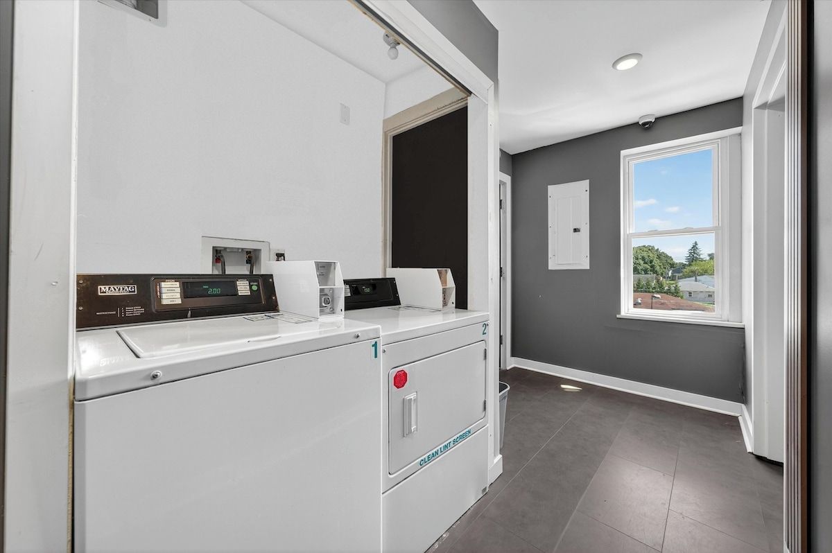 A laundry room with a modern washer and dryer, a small window, and a view of the outside.