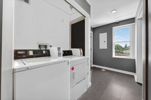 Un lavadero con lavadora y secadora modernas, una ventana pequeña y vistas al exterior.