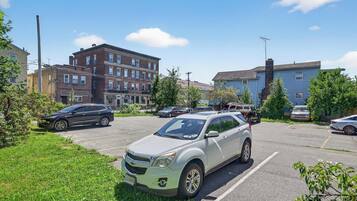A parking lot with several cars, a grassy area, and buildings in the background.