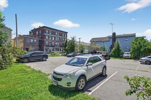 Un estacionamiento con varios autos, un área con césped y edificios al fondo.