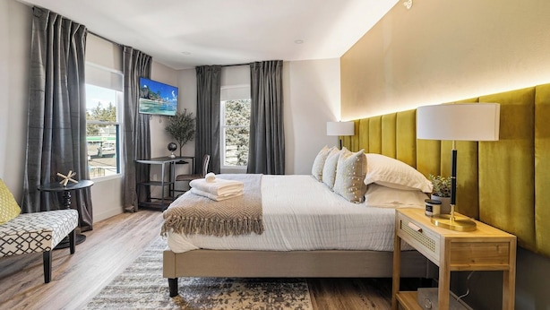 Una camera d'albergo con un letto, comodini, televisione, una finestra con tende e vista sull'esterno.