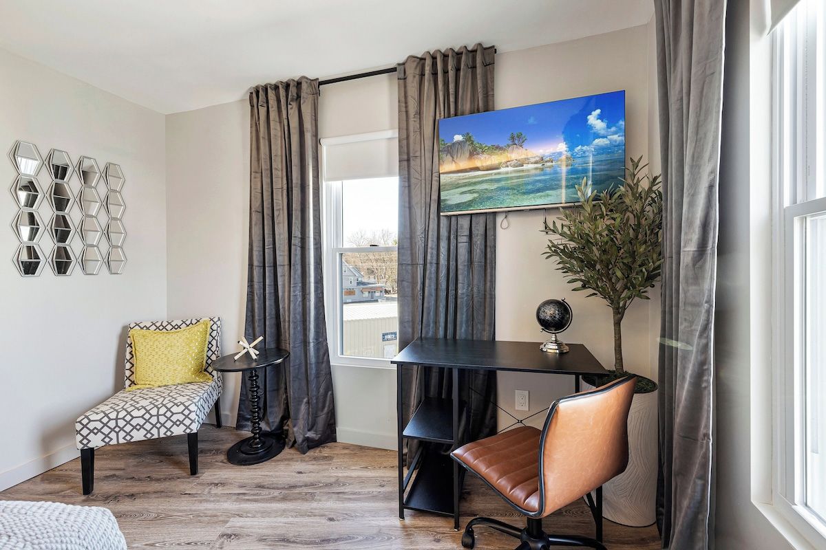 A modern living room with a sofa, a dining table, a TV, and a decorative wall piece.