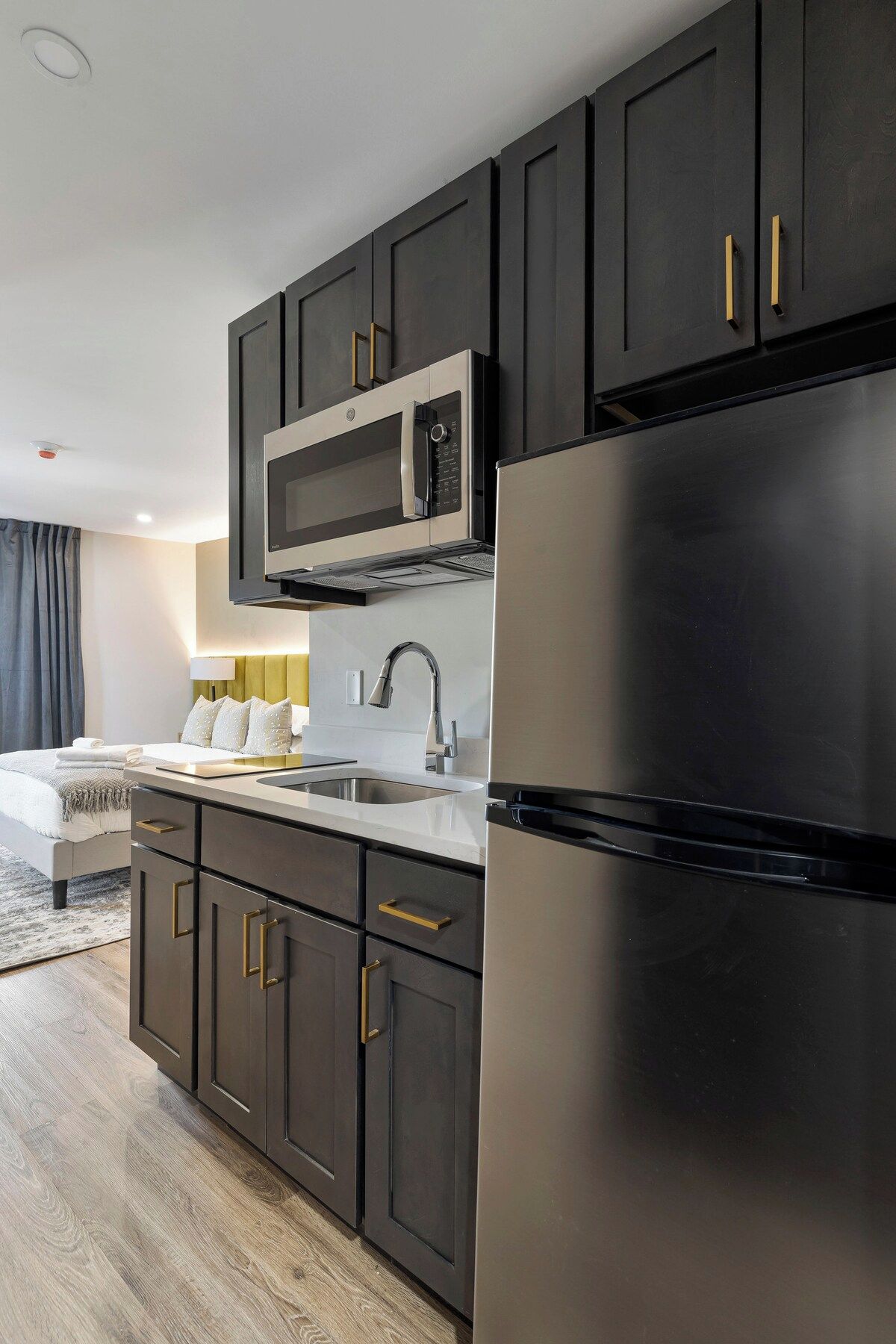 A modern kitchen with dark cabinetry, a stainless steel refrigerator, and a built-in microwave.