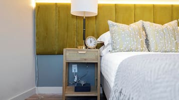 A neatly made bed with patterned pillows, a bedside lamp, and a small wooden nightstand with a clock and a power outlet.